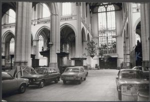 Een zwart-wit foto van het interieur van De Nieuwe Kerk met auto's geparkeerd langs de zuilen.